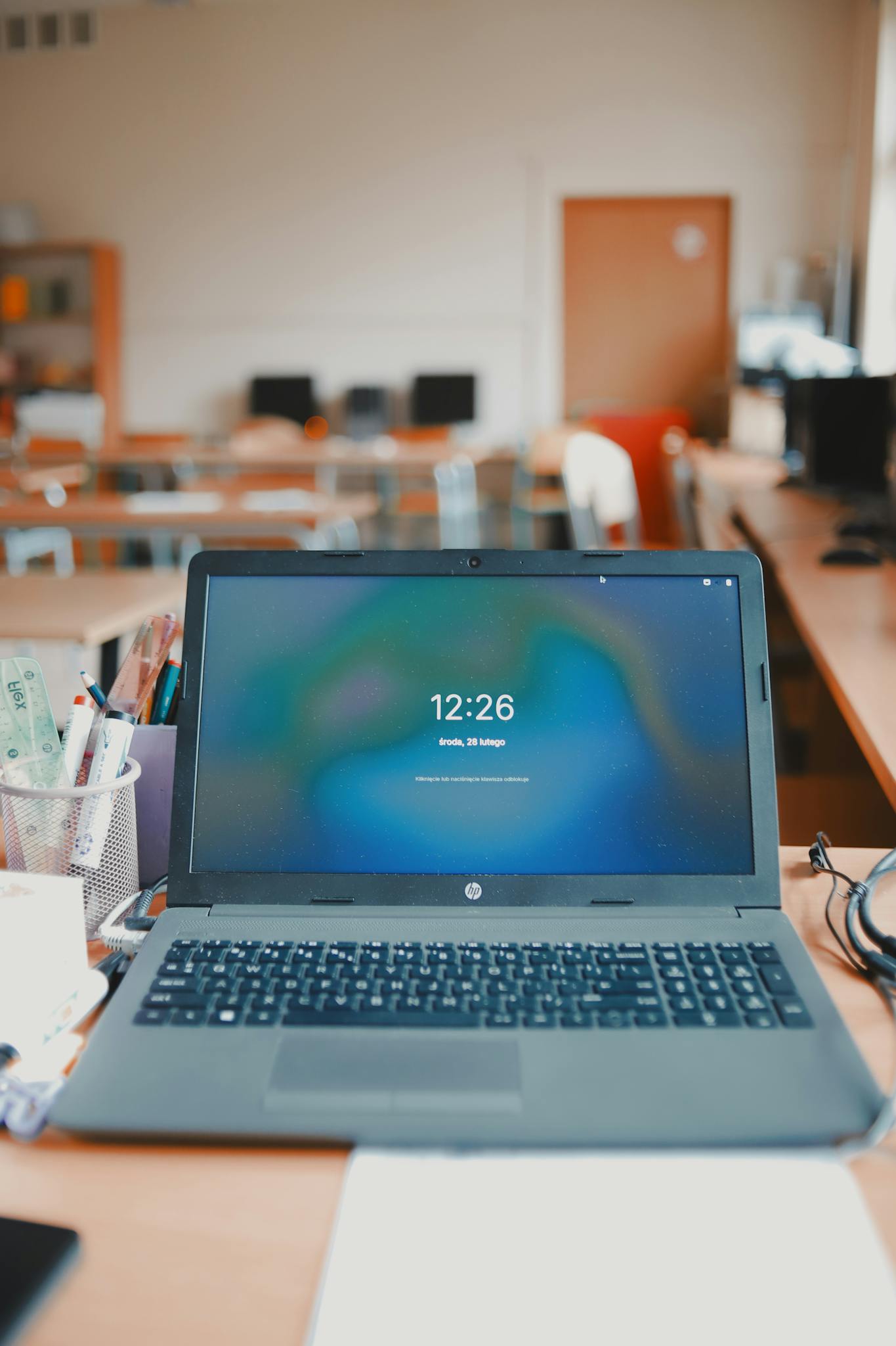 A laptop sits on a desk in a classroom setup, showcasing a modern educational environment.